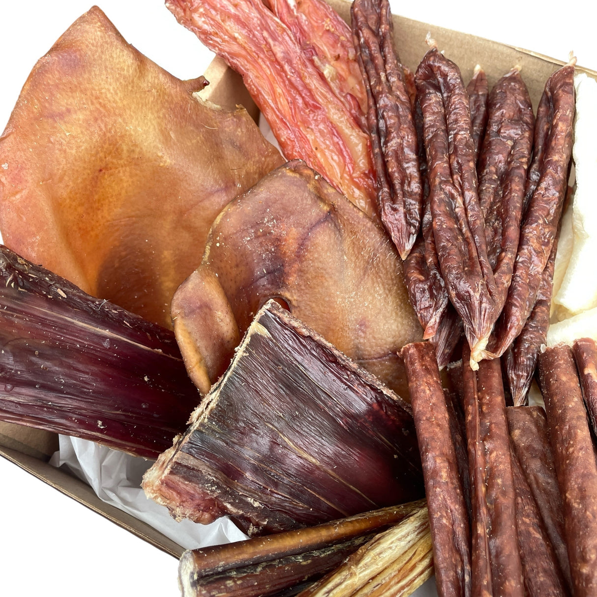 Overhead view of the Puppy’s First Feast, styled as a natural puppy gift set with pig ears, tendons, and meaty strips carefully displayed.